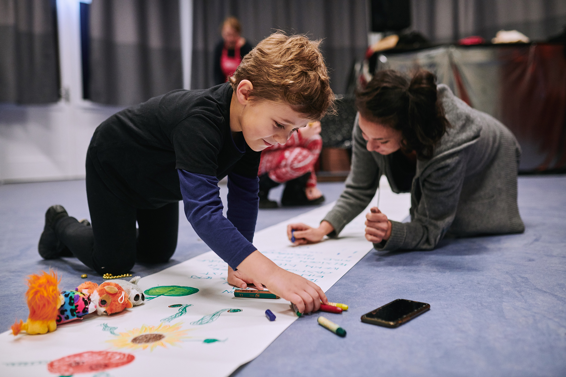 Ein Kind und eine erwachsene Person Knien auf dem Boden und malen etwas.