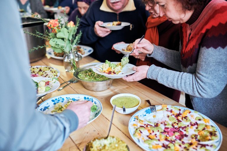 Mehrere erwachsene Personen stehen um einen Buffet-Tisch und bedienen sich mit Speisen.