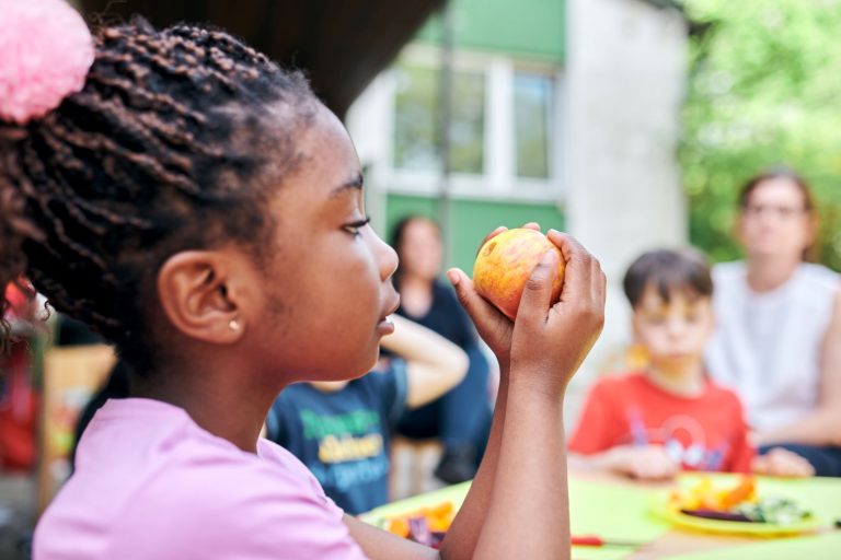 Ein Vorschulkind hält einen Apfel mit einer braunen Stelle in der Hand und betrachtet ihn aufmerksam