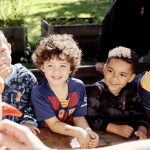 Vier Vorschulkinder betrachten lächelnd krummes und gerettetes Gemüse in den Händen einer mitarbeitenden Person von RESTLOS GLÜCKLICH e. V.