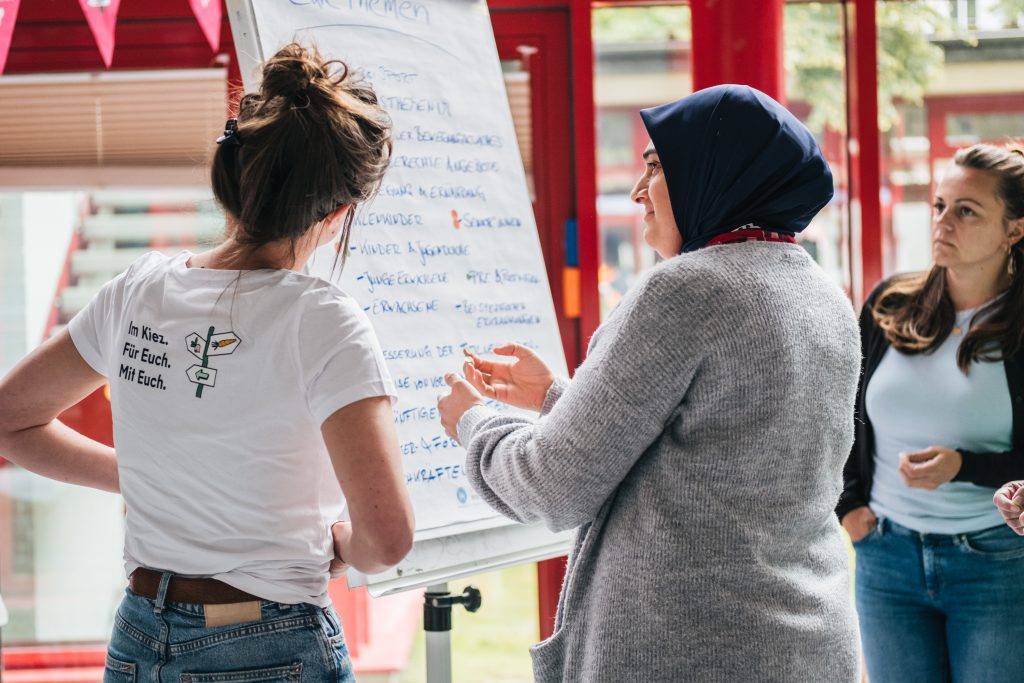 Ann-Kathrin Ridder und zwei teilnehmende Personen stehen vor einem Flipchart und unterhalten sich.