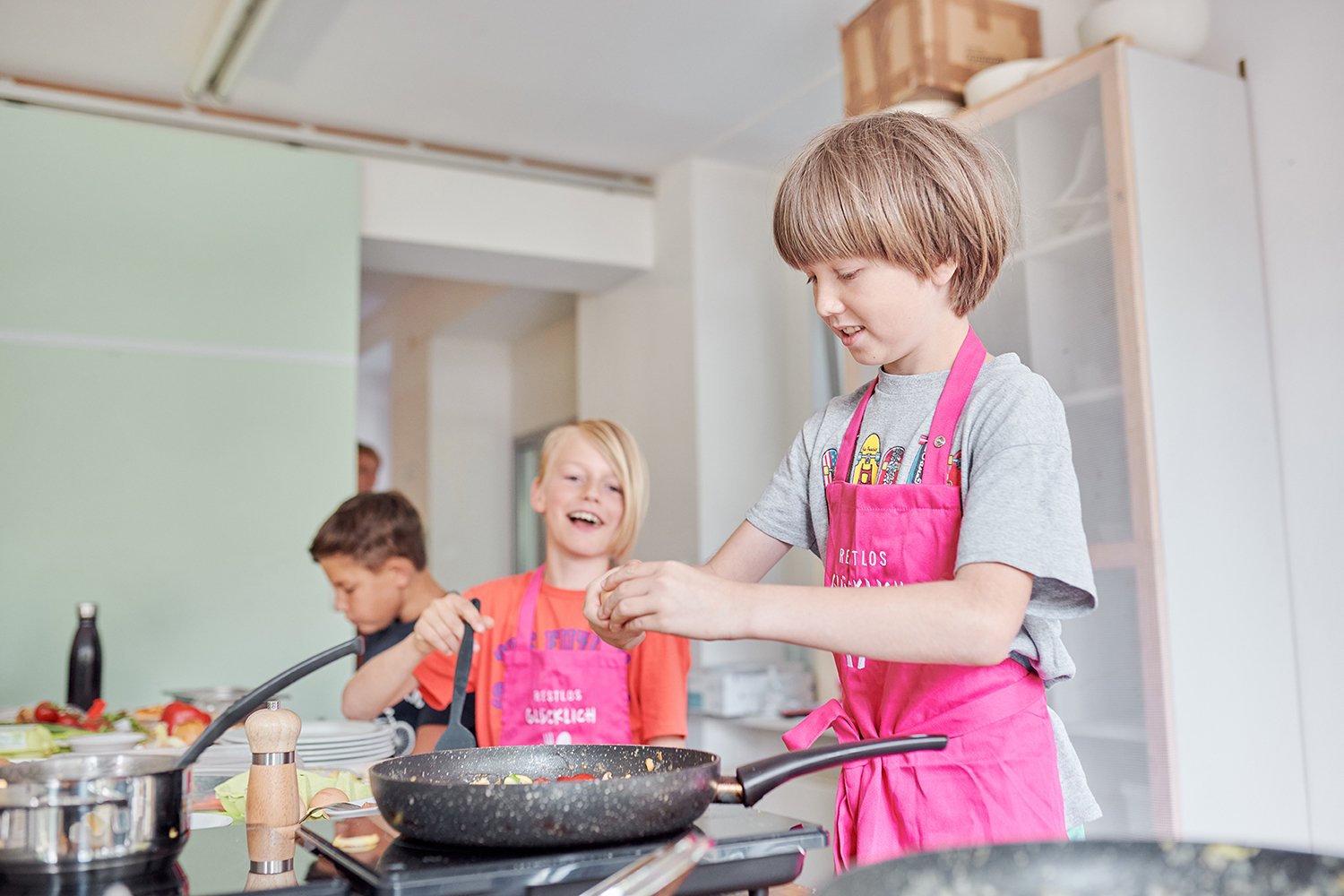 Drei Grundschulkinder stehen am Herd und kochen