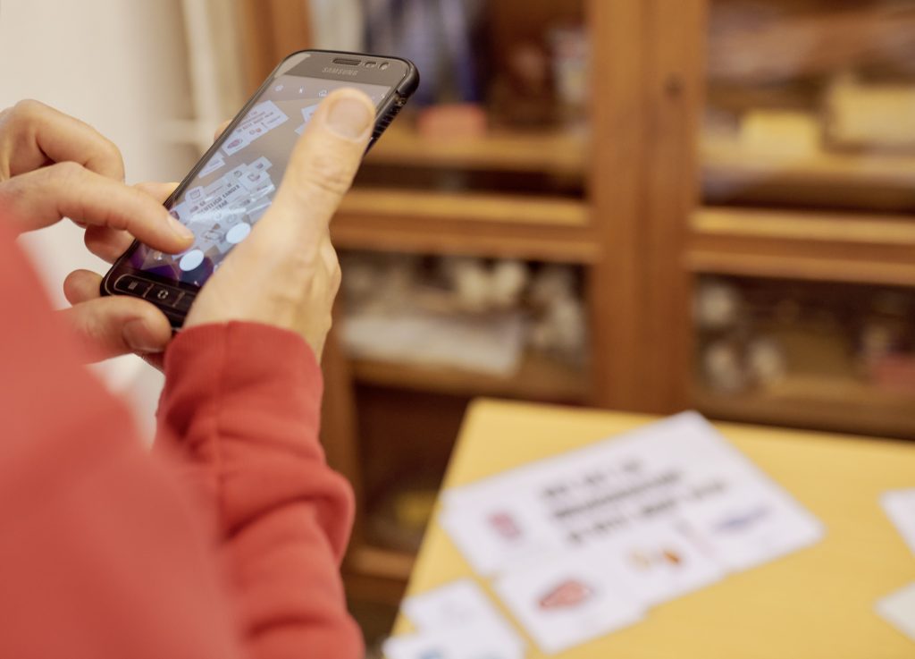 Die Hände einer Person halten ein Handy und machen ein Foto von einem Bildungsspiel