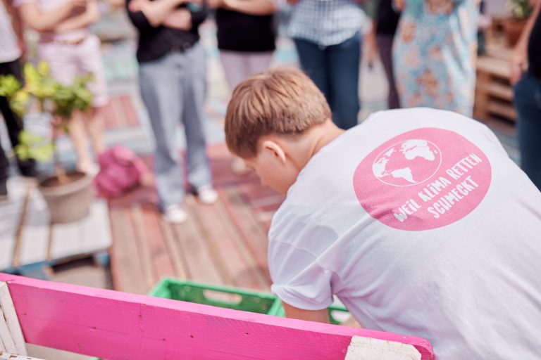 Der Rücken einer mitarbeitenden Person von RESTLOS GLÜCKLICH mit der T-Shirt Aufschrift "Weil Klima retten schmeckt"