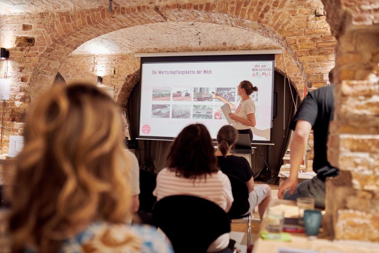 Edith Timm von RESTLOS GLÜCKLICH e. V. hält einen Vortrag. Mehrere Teilnehmende sitzen in Stuhlreihen vor Edith und hören zu.