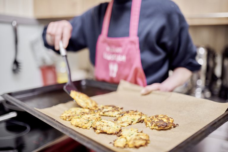 Eine mitarbeitende Person von RESTLOS GLÜCKLICH e. V. platziert mit einem Pfannenheber Kartoffelpuffer auf ein Blech