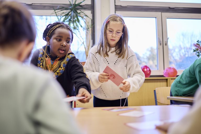 Zwei Grundschülerinnen stehen im Klassenzimmer an einem Tisch und ordnen Karten mit den Schritten zur Lebensmittelwertschätzung in die richtige Reihenfolge.