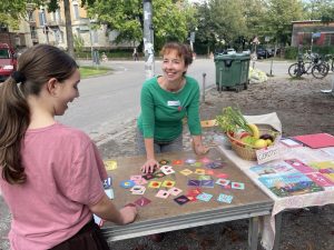 Eine Mitarbeiterin von RESTLOS GLÜCKLICH steht hinter einem Infostand und lacht ein Kind an, das vor dem Infostand steht.