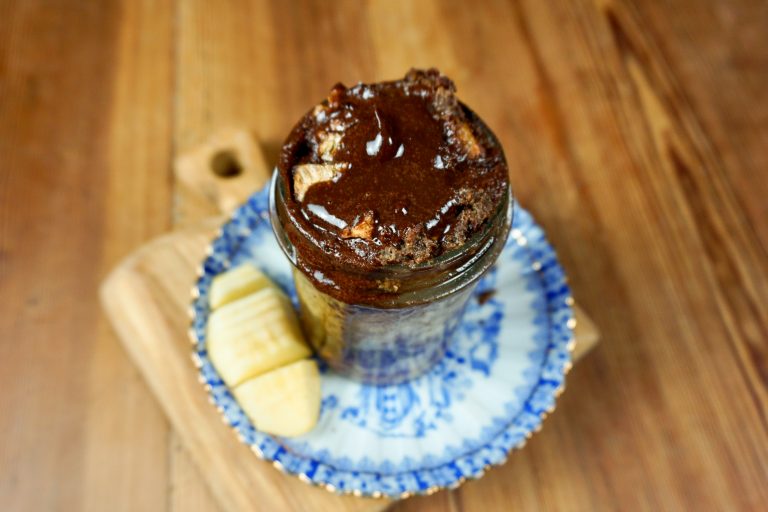 Ein kleines Einmachglas mit einem Brotmuffin-Schokoladen-Dessert steht auf einem kleinen blau-weißen Teller.