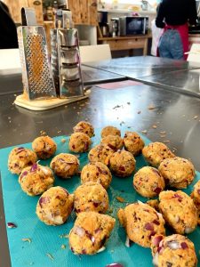 Auf einem Schneidebrett liegen frisch geformte Linsenbällchen, dahinter zeichnen sich Umrisse einer Küche ab.