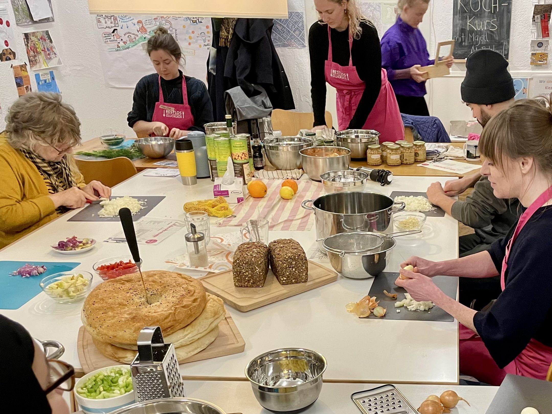 Mehrere Erwachsene sitzen an einem Tisch und schneiden Obst und Gemüse zum Kochen.