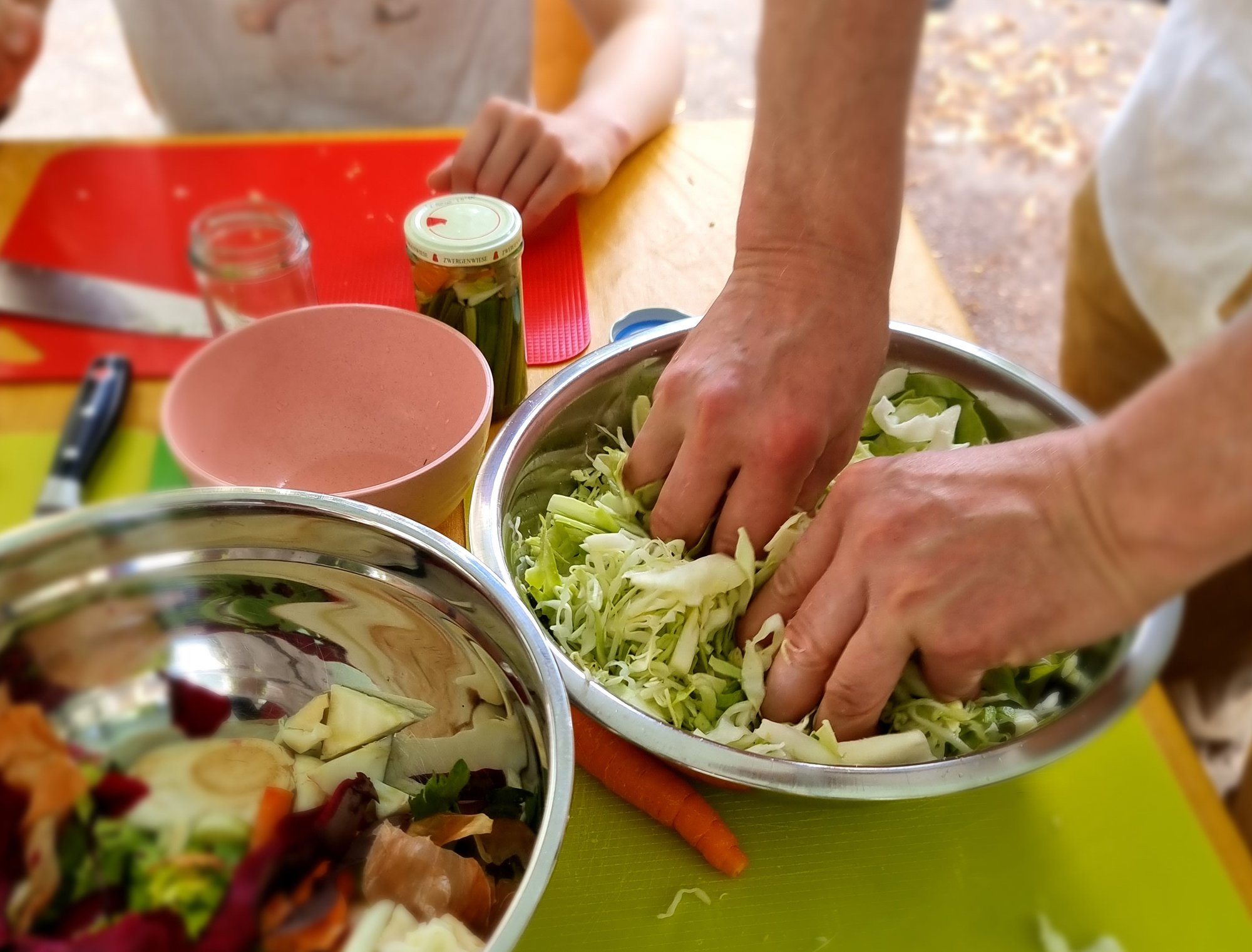 Zwei Hände kneten kleingeschnittenes Sauerkraut in einer großen Schüssel.