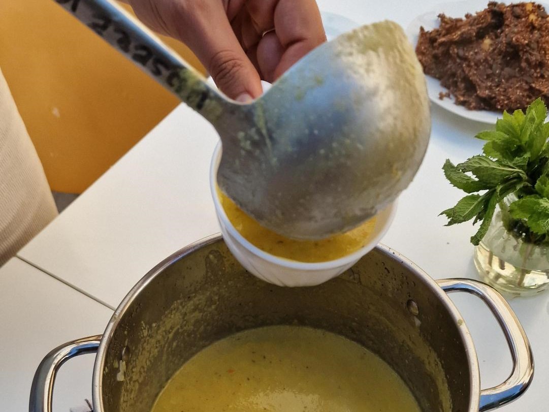 in Topf mit Suppe. Eine Kelle gießt Suppe in eine Tasse.