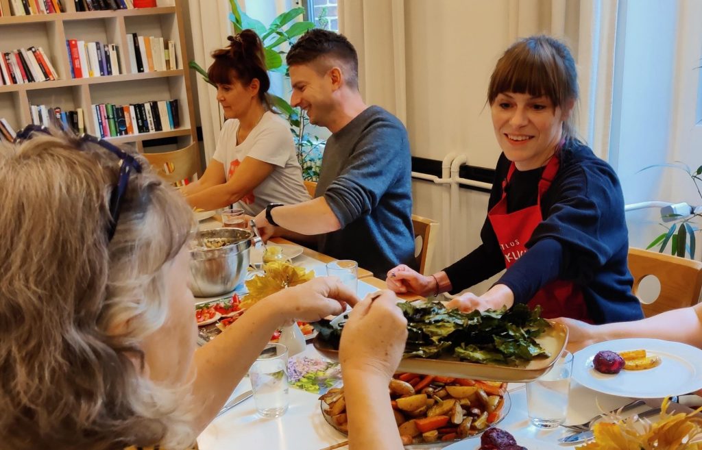 Sechs Erwachsene sitzen an einem Tisch und füllen ihre Teller mit Speisen, die sie zuvor im Koch-Workshop aus geretteten Lebensmitteln selbst zubereitet haben