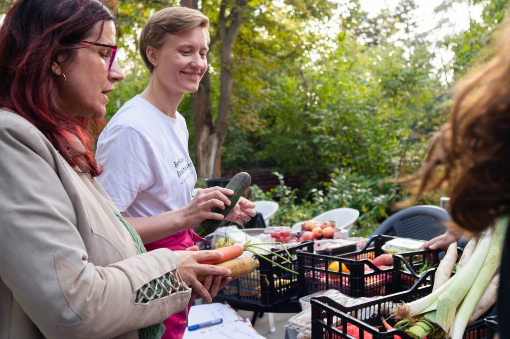 Zwei Frauen stehen an einem Tisch, der mit zahlreichen Kisten voll mit Lebensmitteln gefüllt ist.