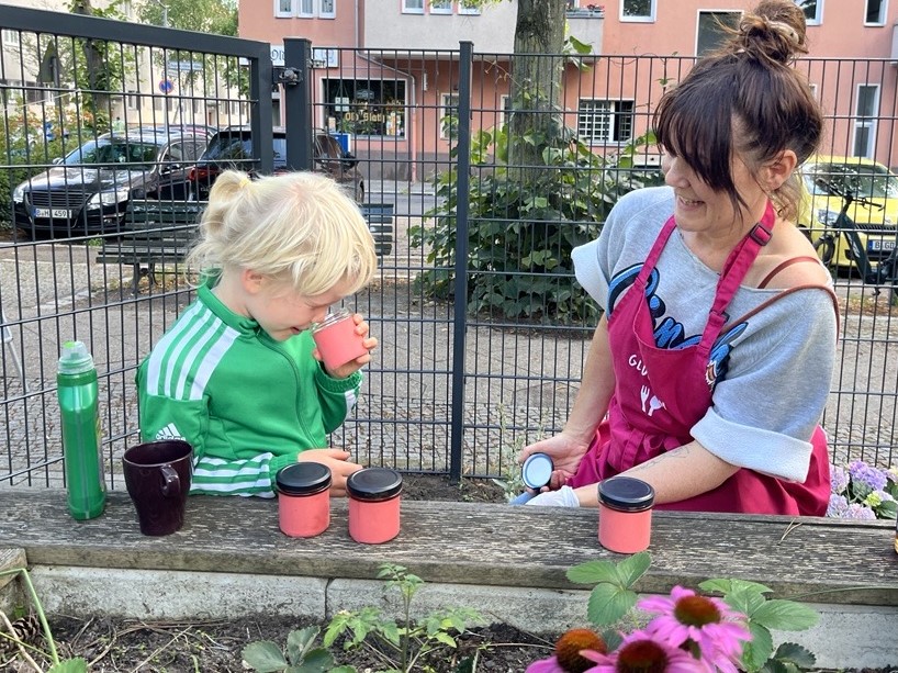 Tanja Krakowski vom Projekt "Prima Klima im AVA-Kiez", wie sie mit einem kleinen Kind draußen auf einer Bank sitzt und ihm Gewürze zum Erraten gibt.