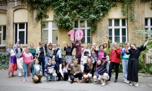 Das Team von RESTLOS GLÜCKLICH posiert in ausgelassener Stimmung mit einer großen, pinken 10 aus Pappe.