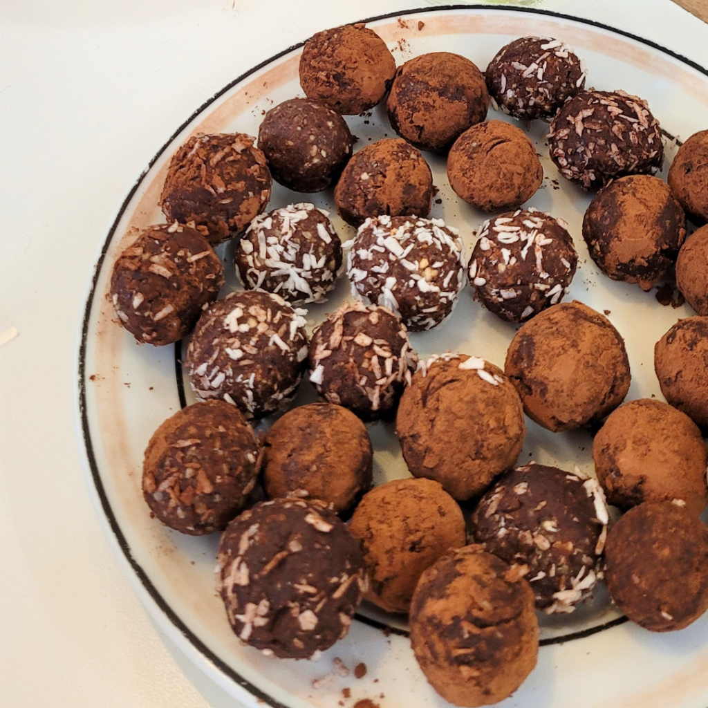 Ein Teller voller selbstgemachter Schoko-Energyballs, dekoriert mit Kokosraspeln und Kakaopulver.