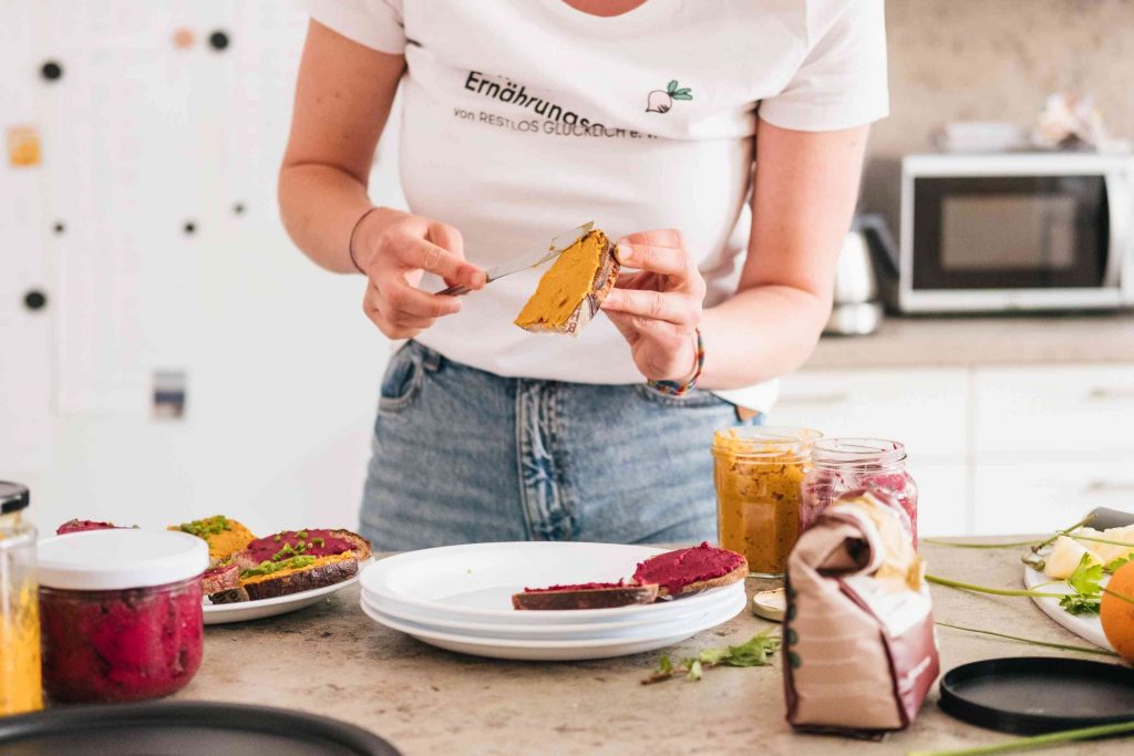 Hände einer mitarbeitenden Person bestreichen eine Scheibe Brot mit Gemüseaufstrich.