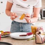 Hände einer mitarbeitenden Person bestreichen eine Scheibe Brot mit Gemüseaufstrich.