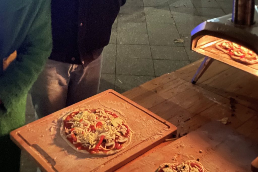 Ein Pizza-Ofen steht im Freihen auf einem Tisch. Davor sind zwei fertige Pizzen auf dem Tisch.