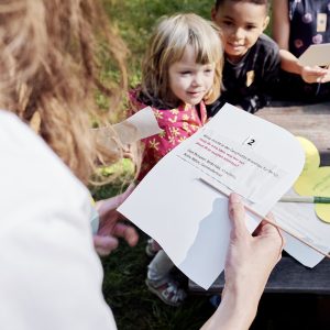 Eine mitarbeitende Person von RESTLOS GLÜCKLICH e. V. liest Vorschulkindern ein Rätsel vor