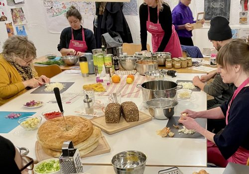 Mehrere Erwachsene sitzen an einem Tisch und schneiden Obst und Gemüse zum Kochen.